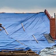 The roofer works on roof when is rain. The tarp covers the roof of the old house in the reconstruction.